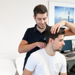 Man in een zwart shirt behandelt een patiuent in een wit shirt met fysiotherapie die onder de basisverzekering vallen zoals hoofdpijn