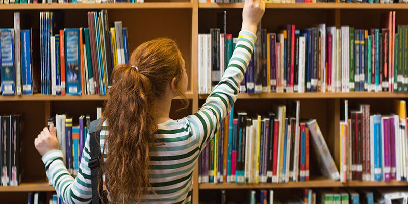 Frozen Shoulder Vrouw pakt een boek uit de kast en heeft last van een Frozen Shoulder